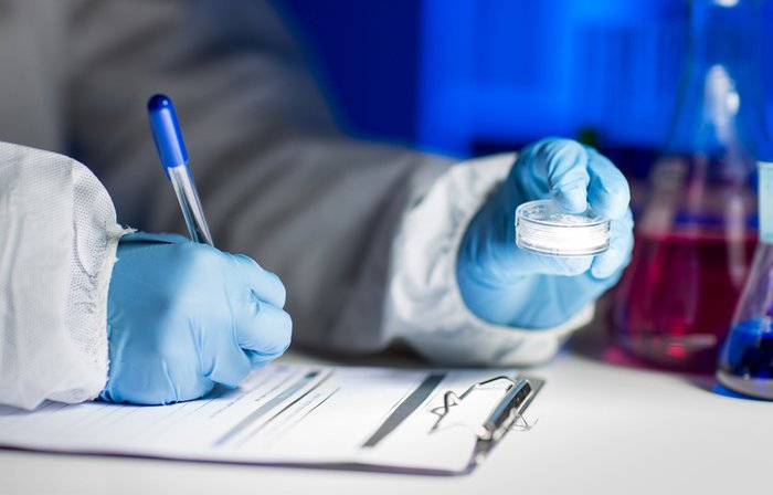 Writing on a notepad while examining a petri dish.