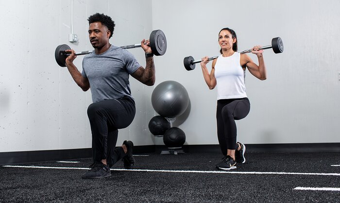 Male and female athletes performing barbell lunges